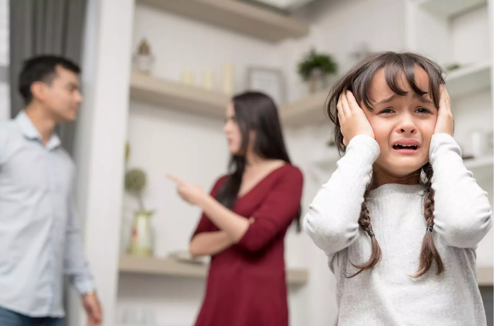 image of man and woman fighting in background while a young girl is holding her hands over her ears and crying in the foreground. 