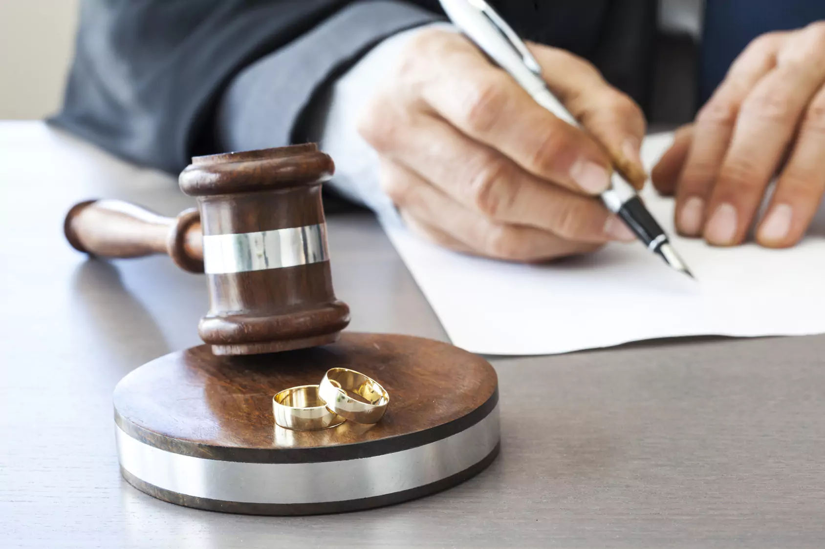 image shows a judge writing on a sheet of paper with a gavel and two wedding bands. The picture symbolizes divorce in Knoxville