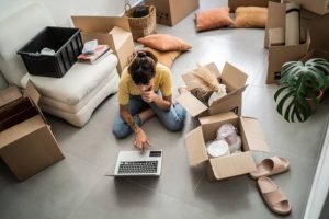 Woman checking laptop to while packing up her property as she moves due to divorce.