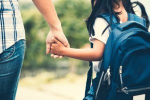 Woman holding hand of school aged child. 